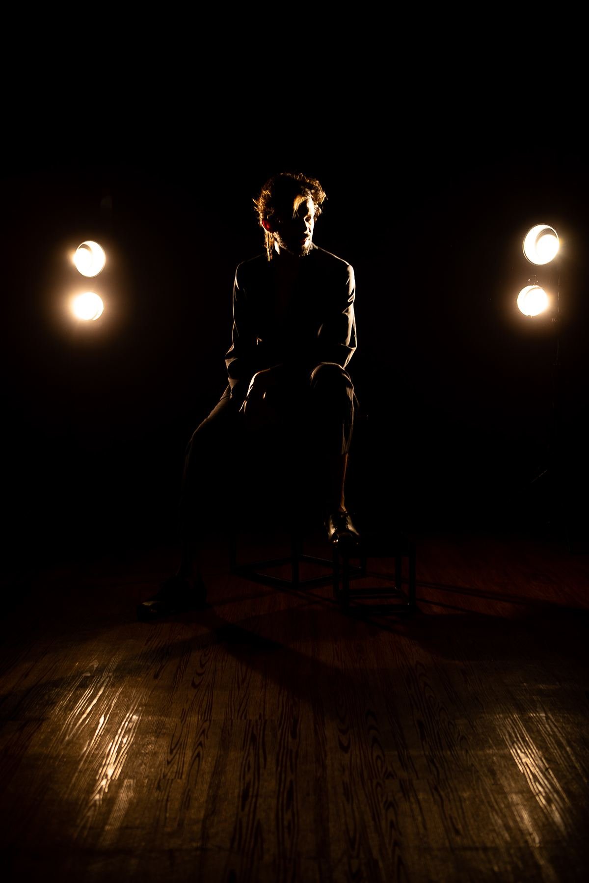 Salomão Soares em silhueta no palco, luzes de teatro